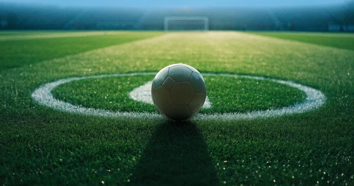 Uma bola de futebol no ponto central de um relvado, à luz da manhã