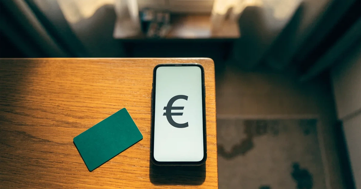 Um telemóvel e um cartão bancário lado a lado numa mesa de madeira, com algumas notas de euro ao lado